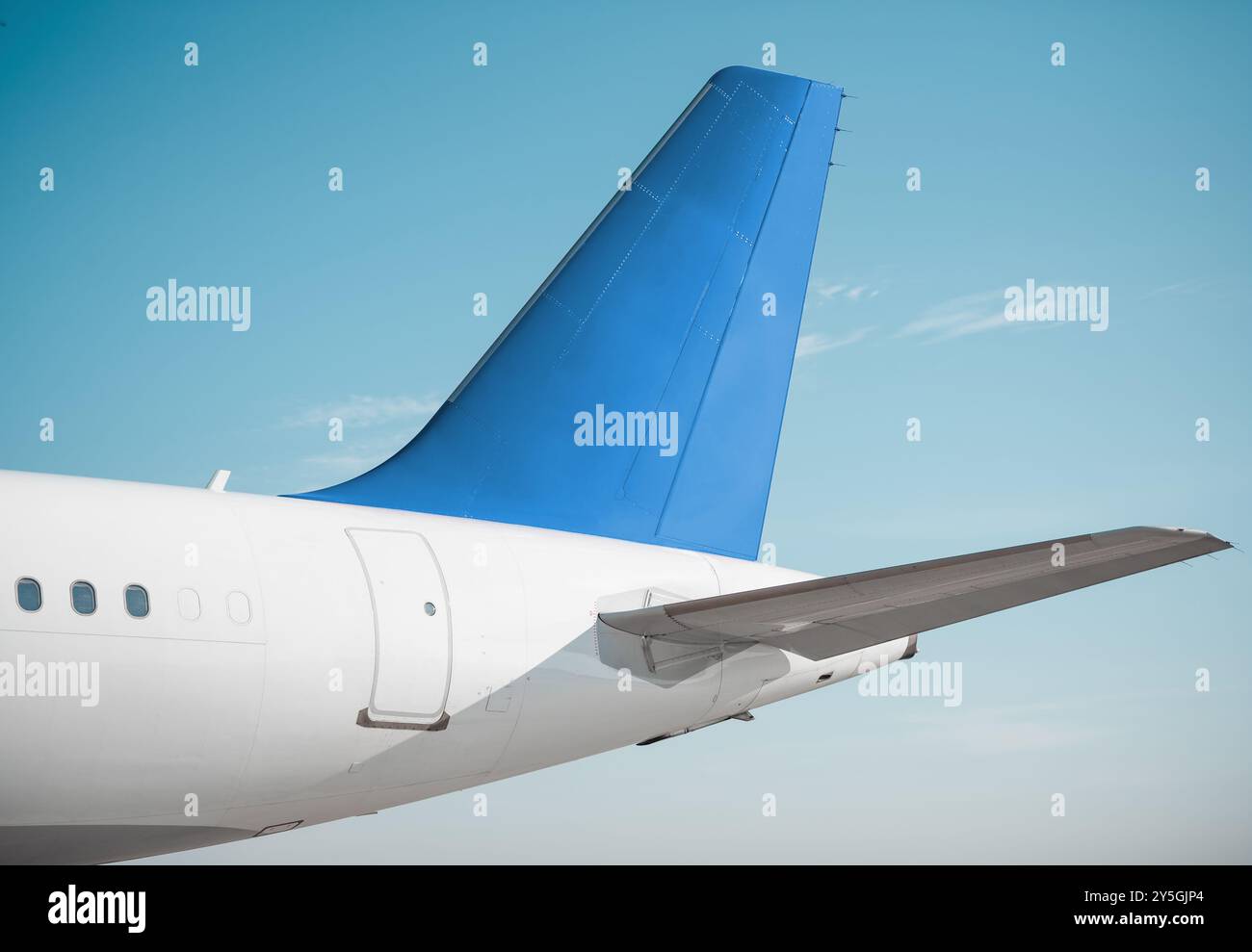 Assemblaggio della coda di un aereo moderno in una giornata di sole. Empennage di aeroplano bianco con stabilizzatore verticale blu, cielo limpido sullo sfondo. Foto Stock