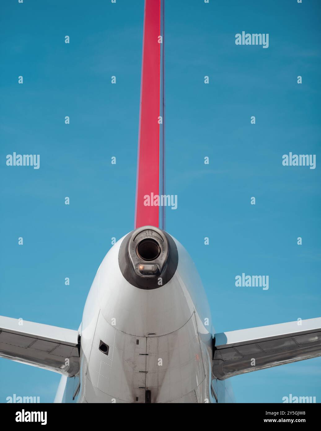Stabilizzatore verticale e unità di potenza ausiliaria (APU) di aeromobili bianchi contro il cielo azzurro. Aeroplano bianco con pinna rossa in una giornata di sole. Foto Stock