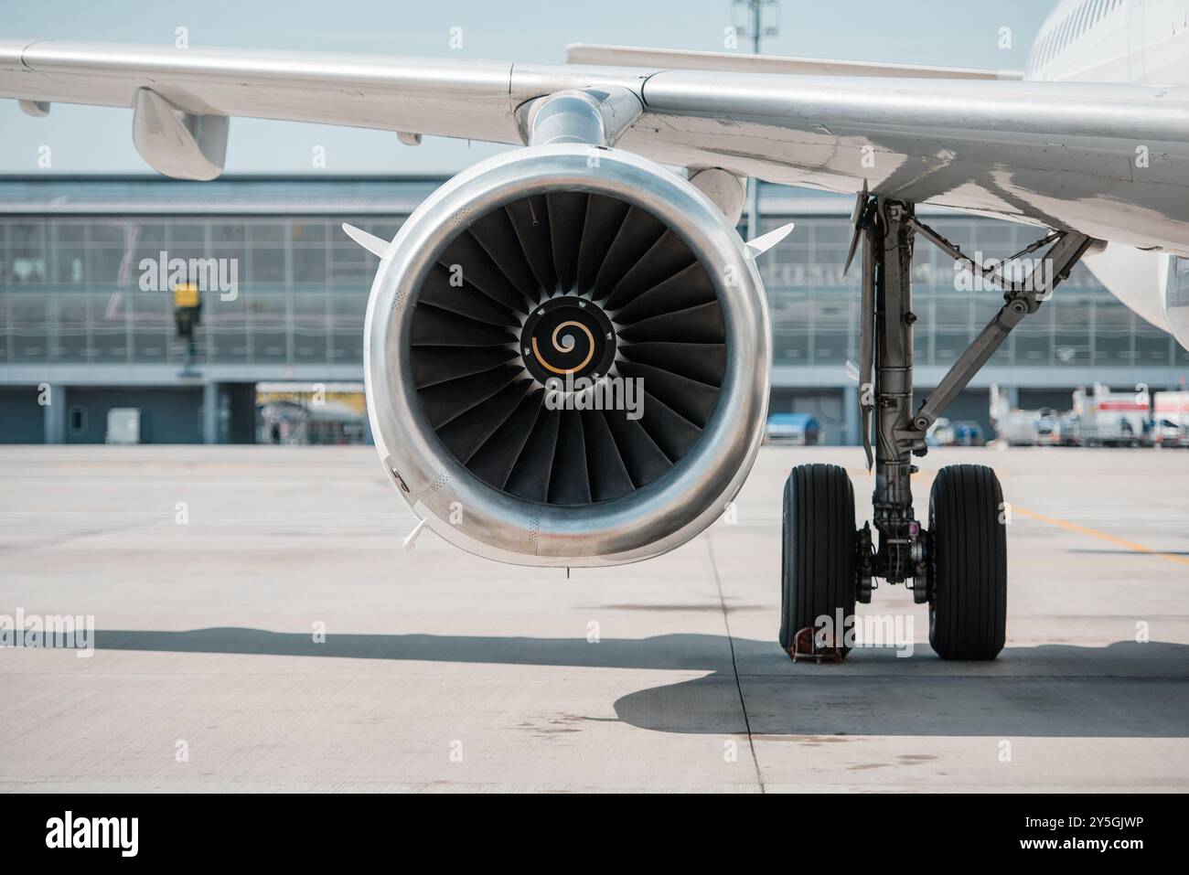 Navicella per motori aerei. Vista frontale del motore turboventilatore sotto un'ala dell'aeromobile passeggeri vicino al carrello di atterraggio. Terminal aeroportuale sullo sfondo. Foto Stock Navicella per motori aerei. Vista frontale del motore turboventilatore sotto un'ala dell'aeromobile passeggeri vicino al carrello di atterraggio. Terminal aeroportuale sullo sfondo. Foto Stock