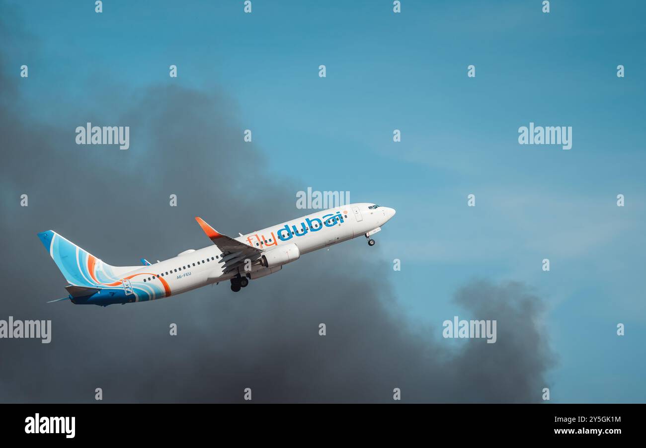 L'aereo flydubai (A6-FEU) decolla mentre il fuoco fuma molto vicino al territorio dell'aeroporto. Vista laterale del Boeing 737 dopo il decollo. Foto Stock