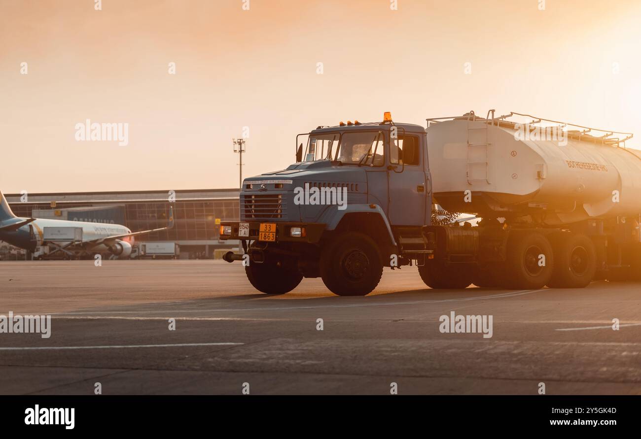 Camion carburante all'aeroporto al tramonto. Rifornimento aereo sulla piattaforma KrAZ per camion. Terminal aeroportuale sullo sfondo. Foto Stock