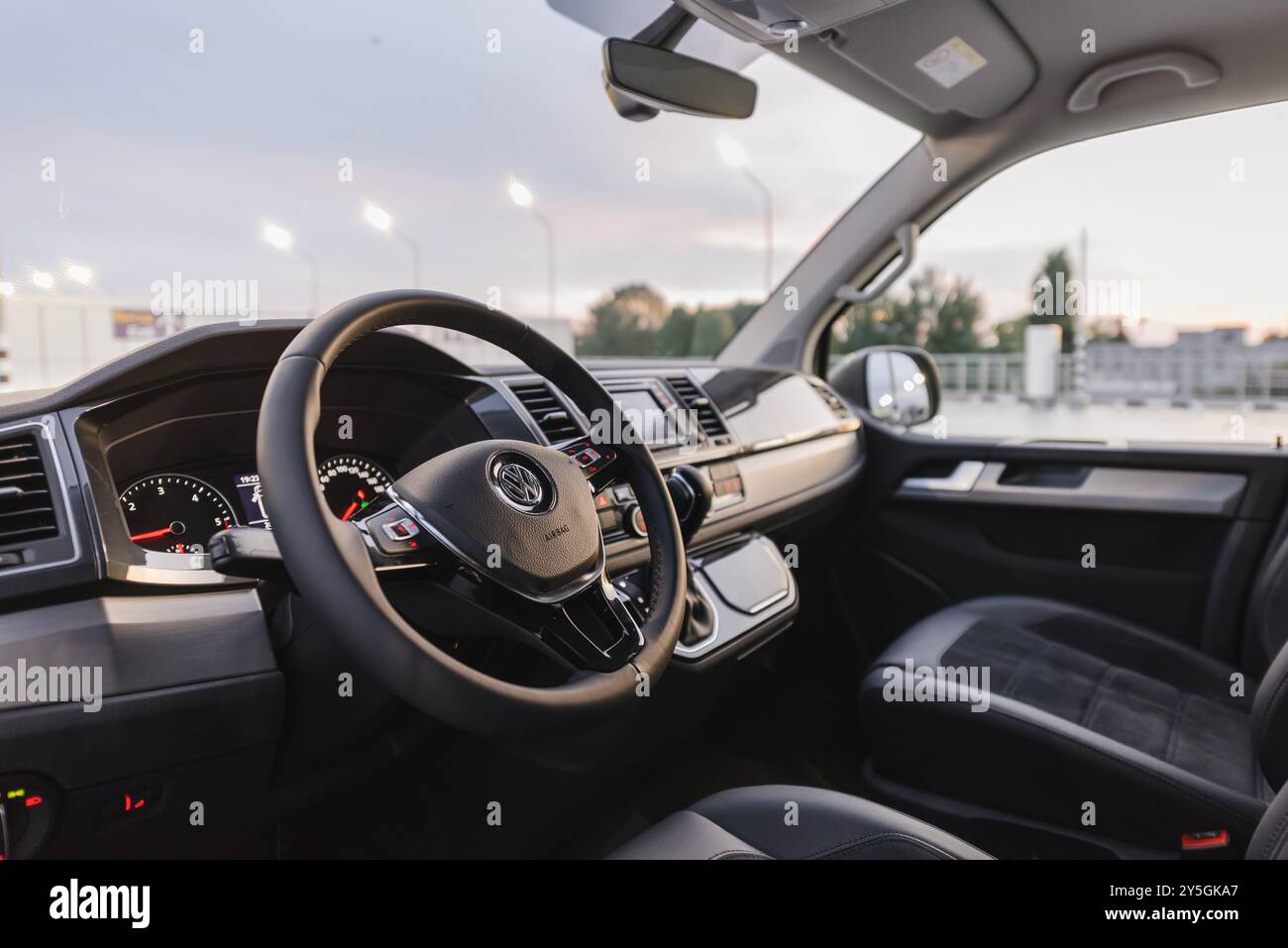 Interno della Volkswagen Transporter al crepuscolo. Prima fila di sedili e cruscotto del pulmino VW T6 al piano superiore del garage. Foto Stock