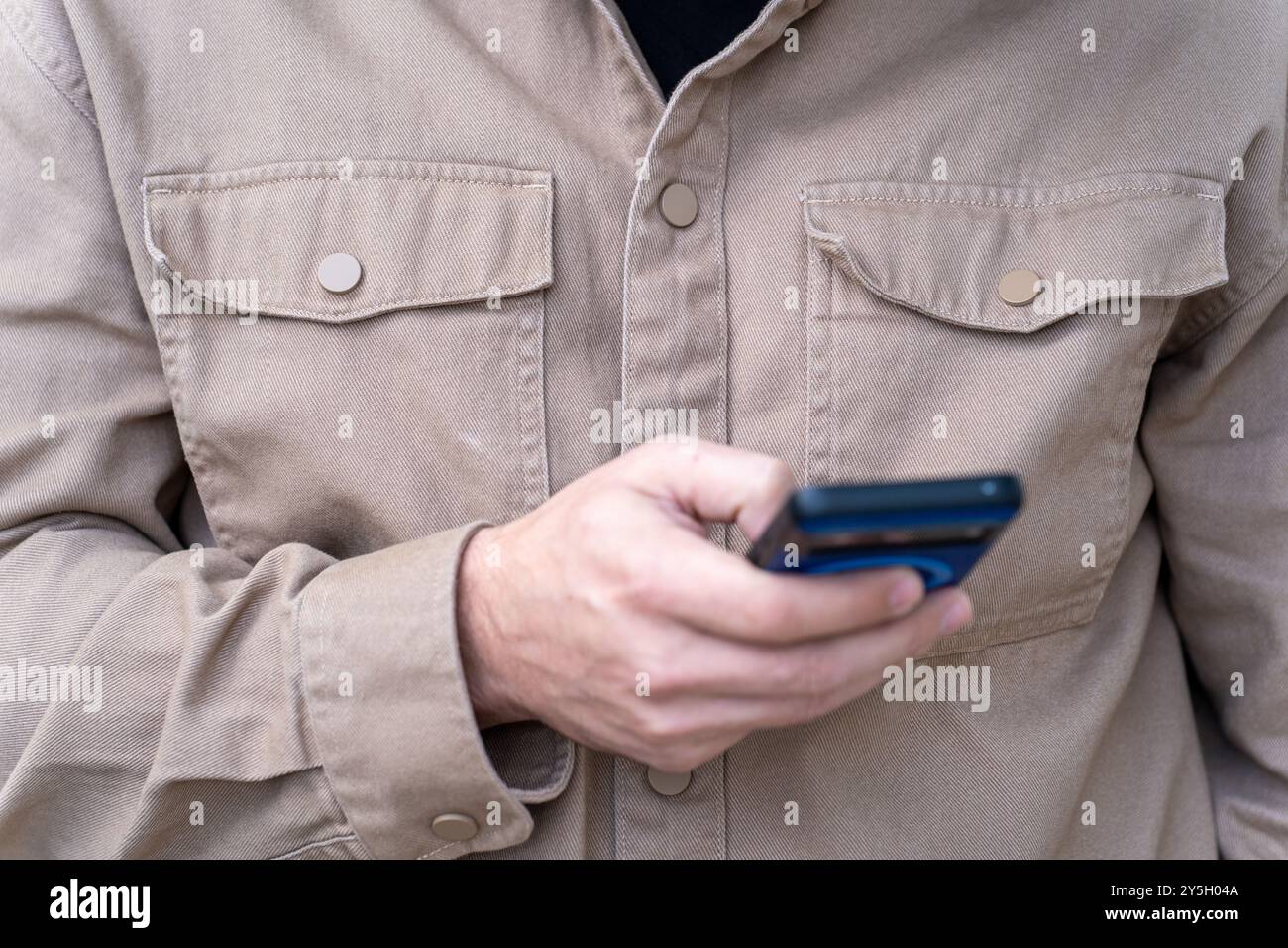 T-Shirt uomo in marrone che controlla il telefono cellulare per messaggi: Routine quotidiana e concetto di dipendenza tecnologica Foto Stock