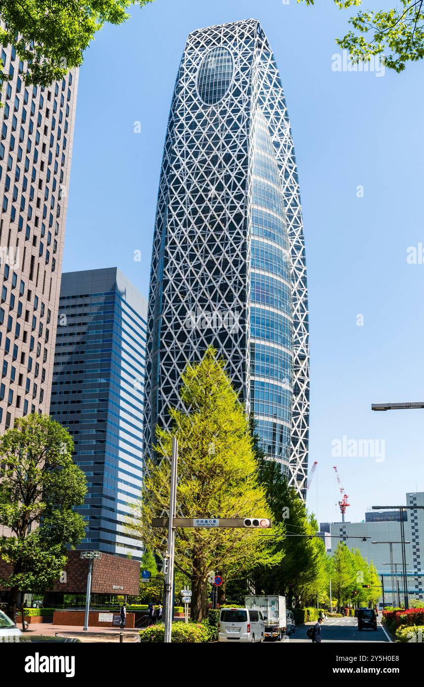 Il caratteristico edificio Tokyo Mode Gakuen moderno con struttura in vetro e acciaio a Shinjuku, con alberi verdi primaverili davanti e un cielo azzurro e limpido dietro. Foto Stock