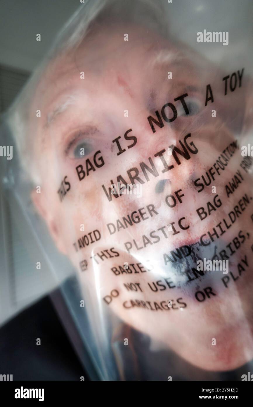 Primo piano di un anziano uomo maturo, soffocato in un sacchetto di plastica trasparente con avviso di avvertimento stampato 2024, USA Foto Stock