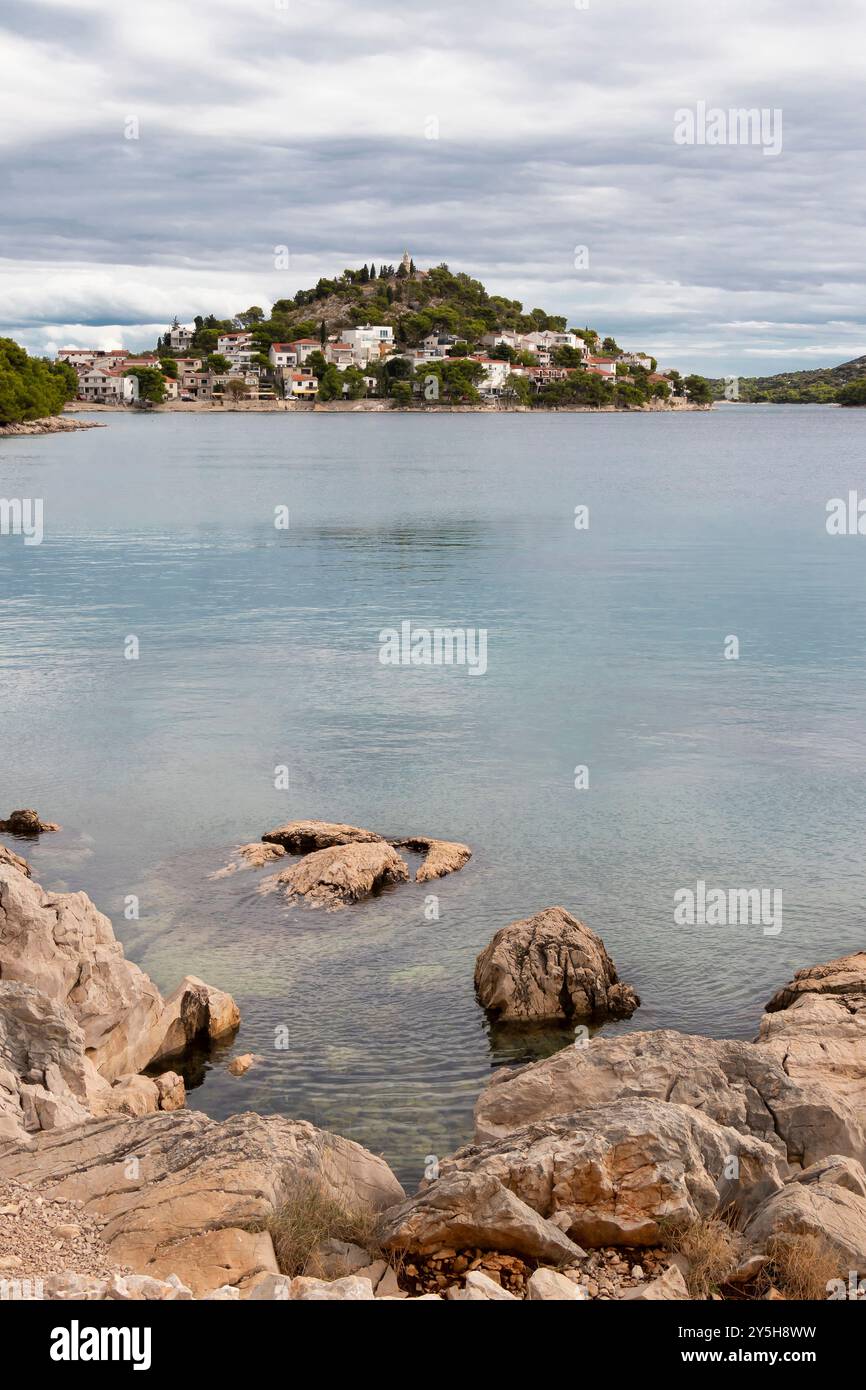 Tribunj, Croazia - 13 settembre 2024: Spiaggia rocciosa e collina con la chiesa di San Nicola sullo sfondo Foto Stock