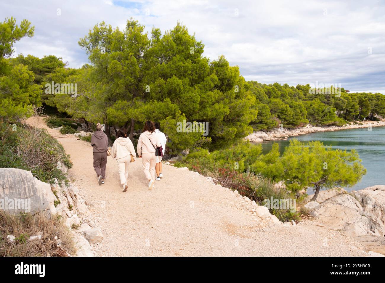 Tribunj, Croazia - 13 settembre 2024: Persone che camminano lungo il sentiero costiero nella pineta vicino al mare roccioso Foto Stock