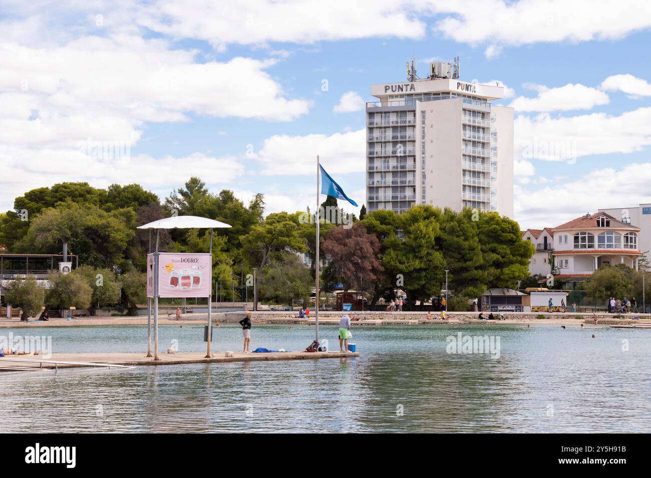 Vodice, Croazia - 14 settembre 2024: Torre di salvaguardia e bandiera sul molo della spiaggia blu e hotel Punta sullo sfondo Foto Stock