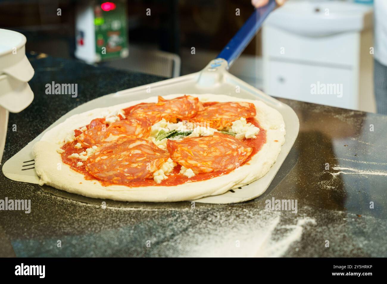 Lo chef prepara e distribuisce l'impasto su una pala per pizza prima di metterlo in forno Foto Stock