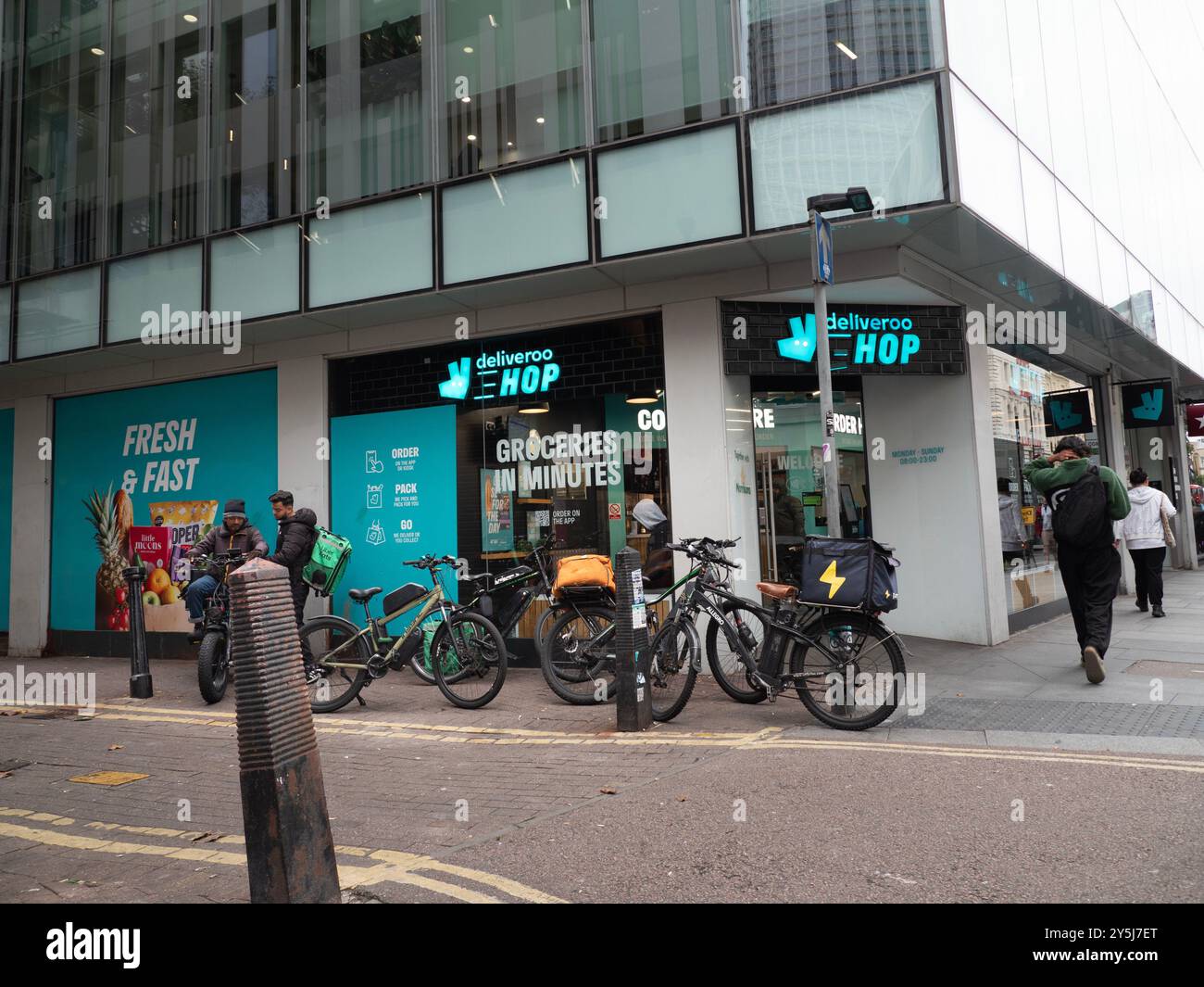 Consegna del cibo i ciclisti si riuniscono all'esterno del negozio di alimentari Deliveroo Hop, nel centro di Londra, Regno Unito Foto Stock