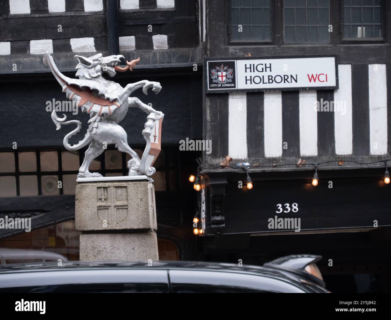 Primo piano del cartello di High Holborn Street con il cartello di confine del drago della City of London di fronte all'edificio originale in legno Tudor, lo Staple Inn Foto Stock