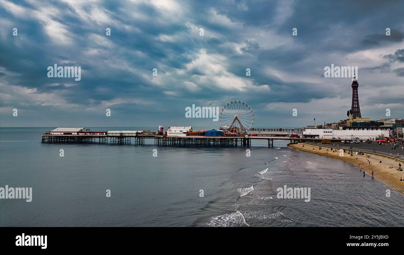 Una vista panoramica di un molo che si estende nel mare calmo, caratterizzato da una grande ruota panoramica e un'alta torre sullo sfondo. Il cielo è coperto di dramma Foto Stock