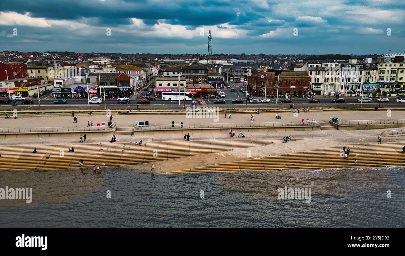 Vista aerea di una passeggiata sul mare con persone che camminano e si rilassano lungo la riva. La spiaggia presenta scalini di legno che conducono all'acqua e un Foto Stock