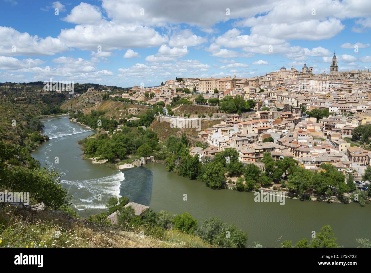 Panorama di una città su una collina con un fiume in primo piano e molte case sotto un cielo blu con nuvole, Toledo, il fiume Tago, Castilla-la Mancha, Spa Foto Stock