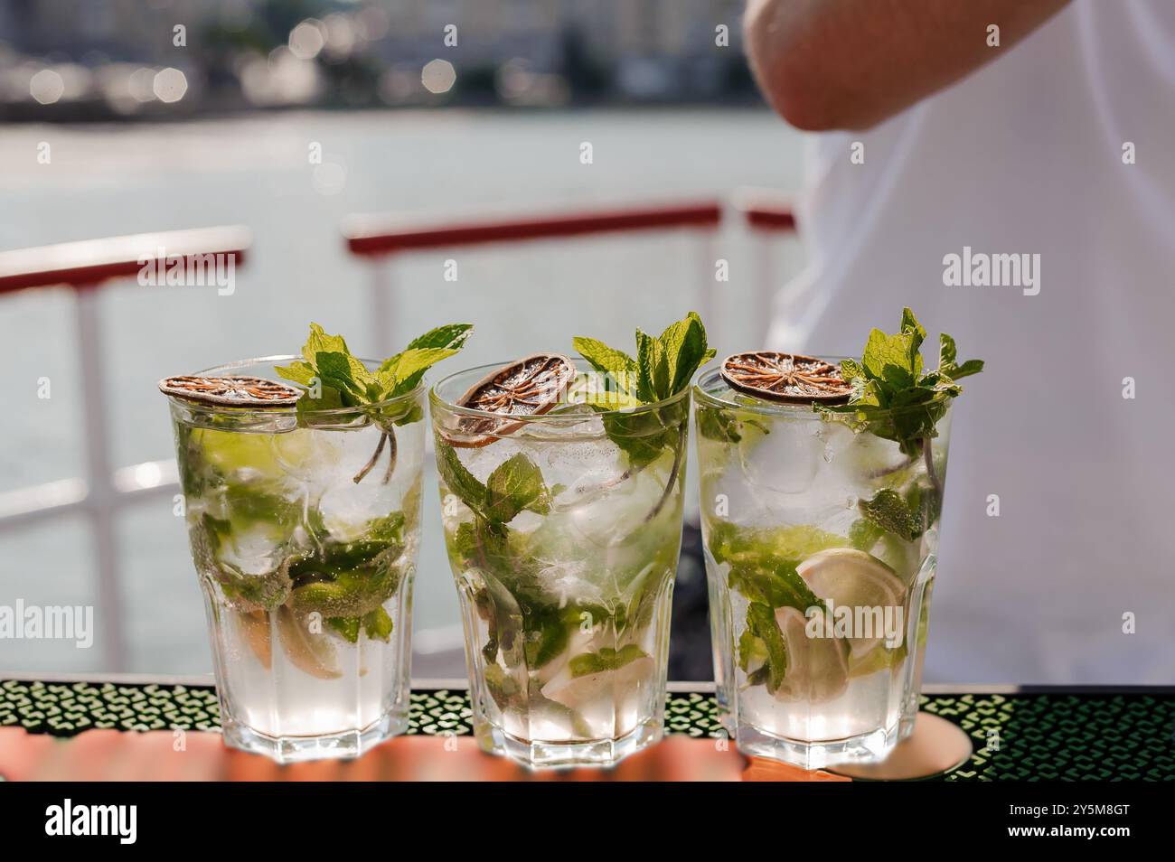 Rinfrescanti cocktail Mojito con Menta e Lime Garnish serviti in bicchieri trasparenti in un Sunny Day by the Water. Foto Stock