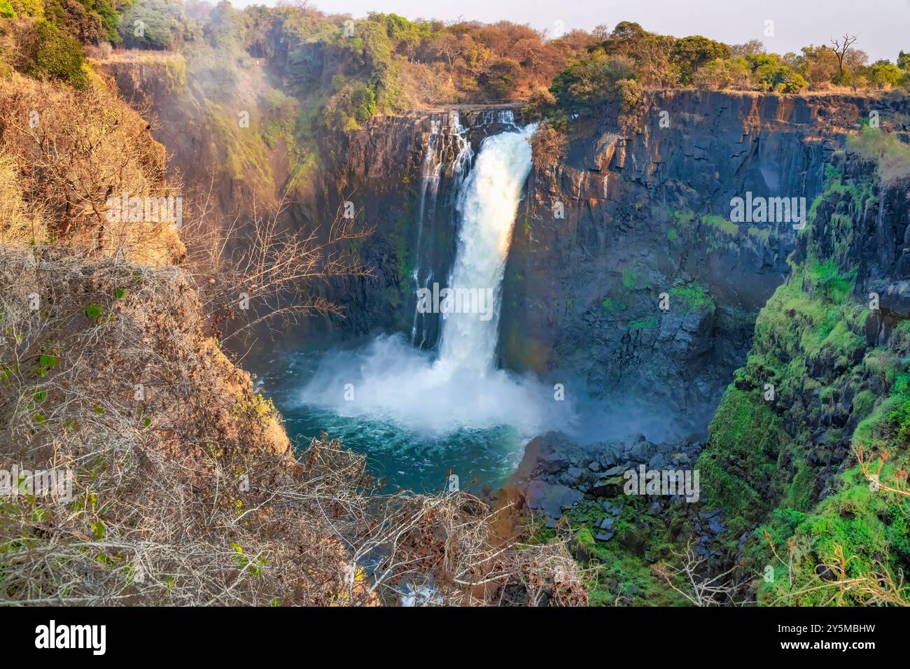 Potente cascata che si tuffa in una tranquilla piscina, circondata da vegetazione lussureggiante e scogliere aspre in una giornata luminosa e soleggiata come parte delle Cascate Vittoria Foto Stock