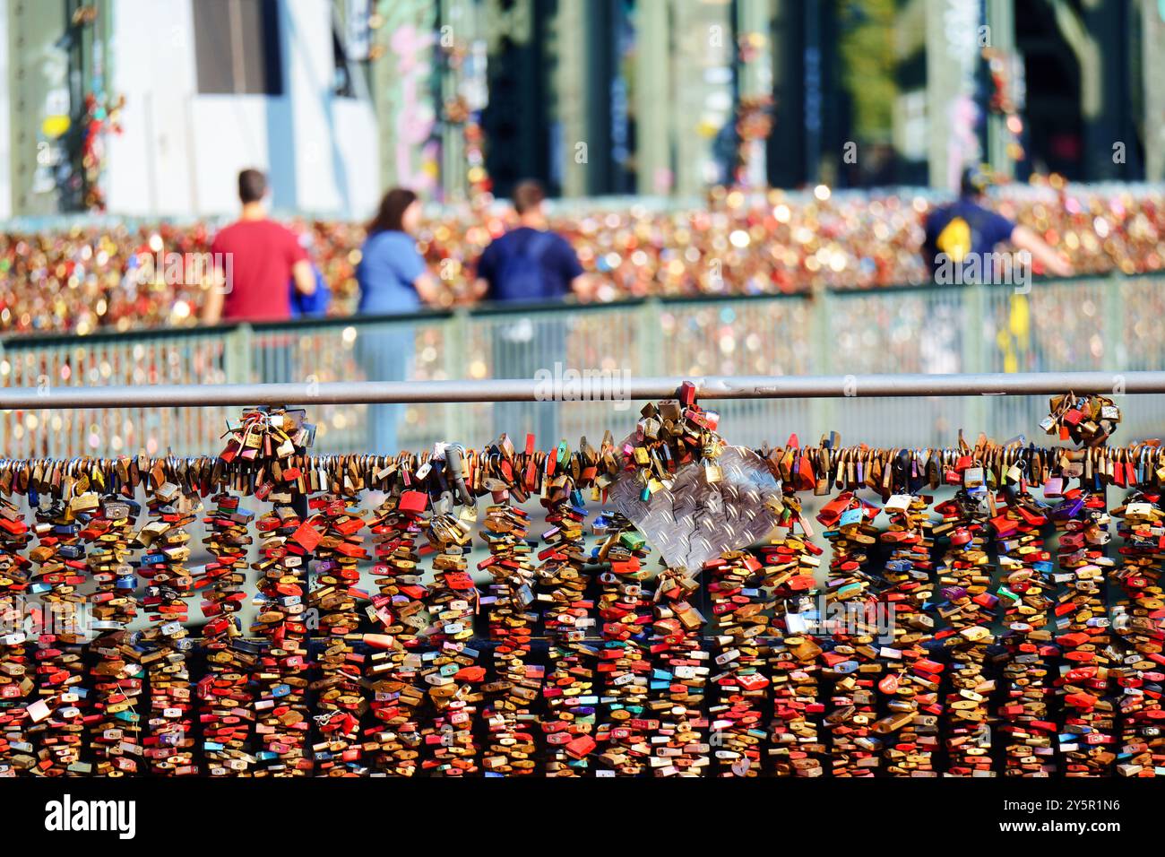 migliaia di chiuse d'amore sulle ringhiere del ponte hohenzollern nella città vecchia di colonia con turisti e treni sullo sfondo sfocato Foto Stock