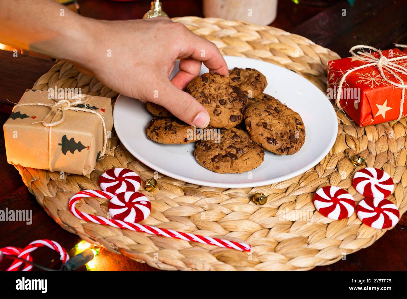 Maschio che afferra a mano il biscotto di Natale da un piatto circondato da decorazioni natalizie Foto Stock