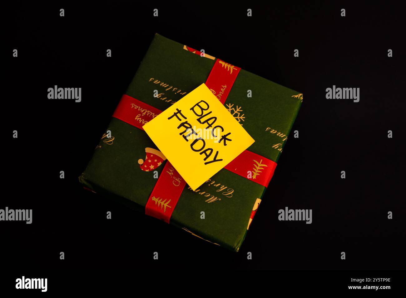 Regalo di Natale verde con un messaggio su un foglio giallo che dice Black Friday su sfondo nero, concetto di shopping natalizio Foto Stock Regalo di Natale verde con un messaggio su un foglio giallo che dice Black Friday su sfondo nero, concetto di shopping natalizio Foto Stock