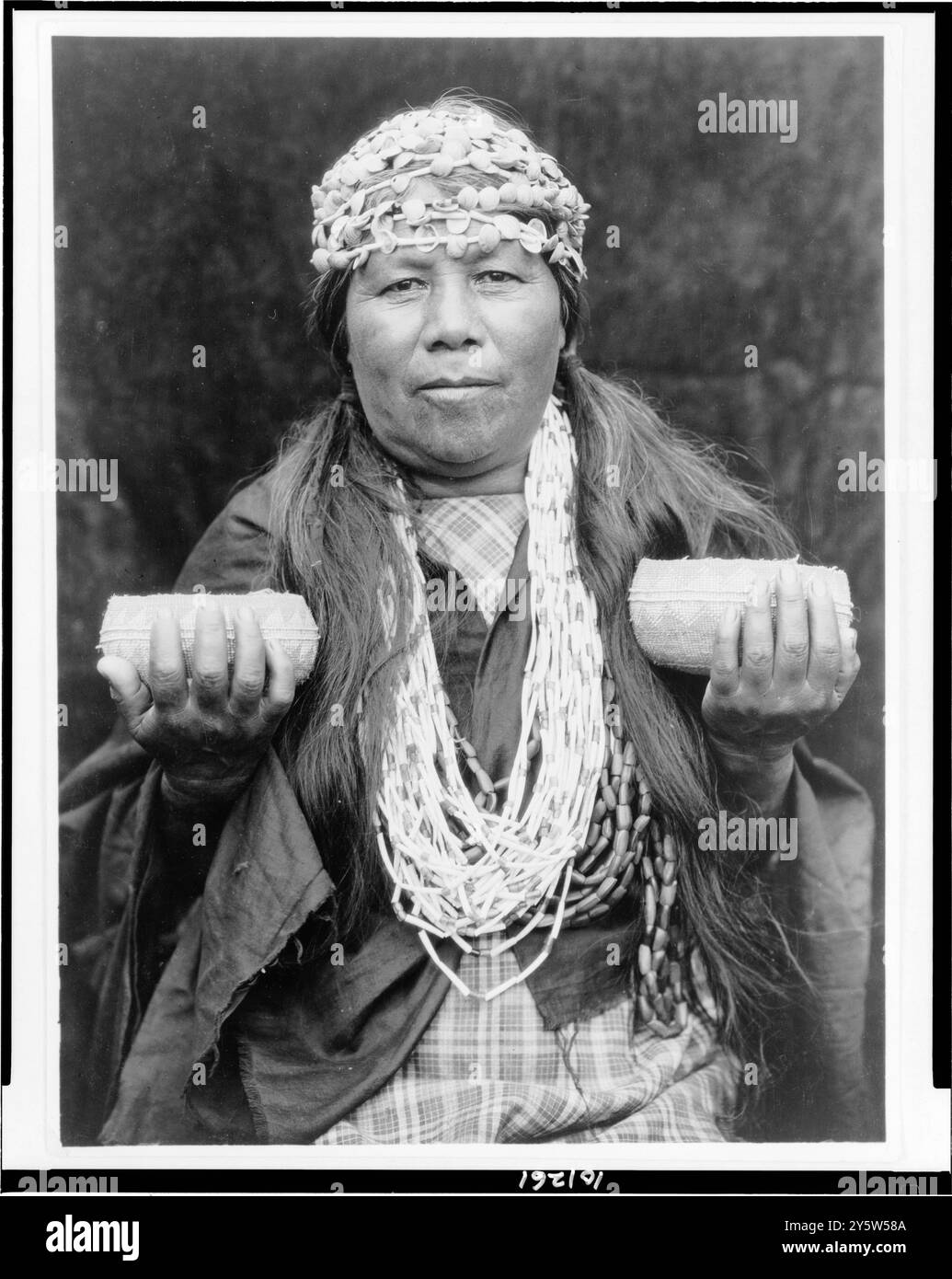Shaman Hupa femminile. STATI UNITI. C. 1923 di E.S. Curtis, 1868-1952, fotografa Athapascan Hupa Woman di Athapascan Hupa Woman, ritratto a mezza lunghezza, in piedi, rivolto verso la parte anteriore, con archetti a guscio, collana e due cesti. Foto Stock