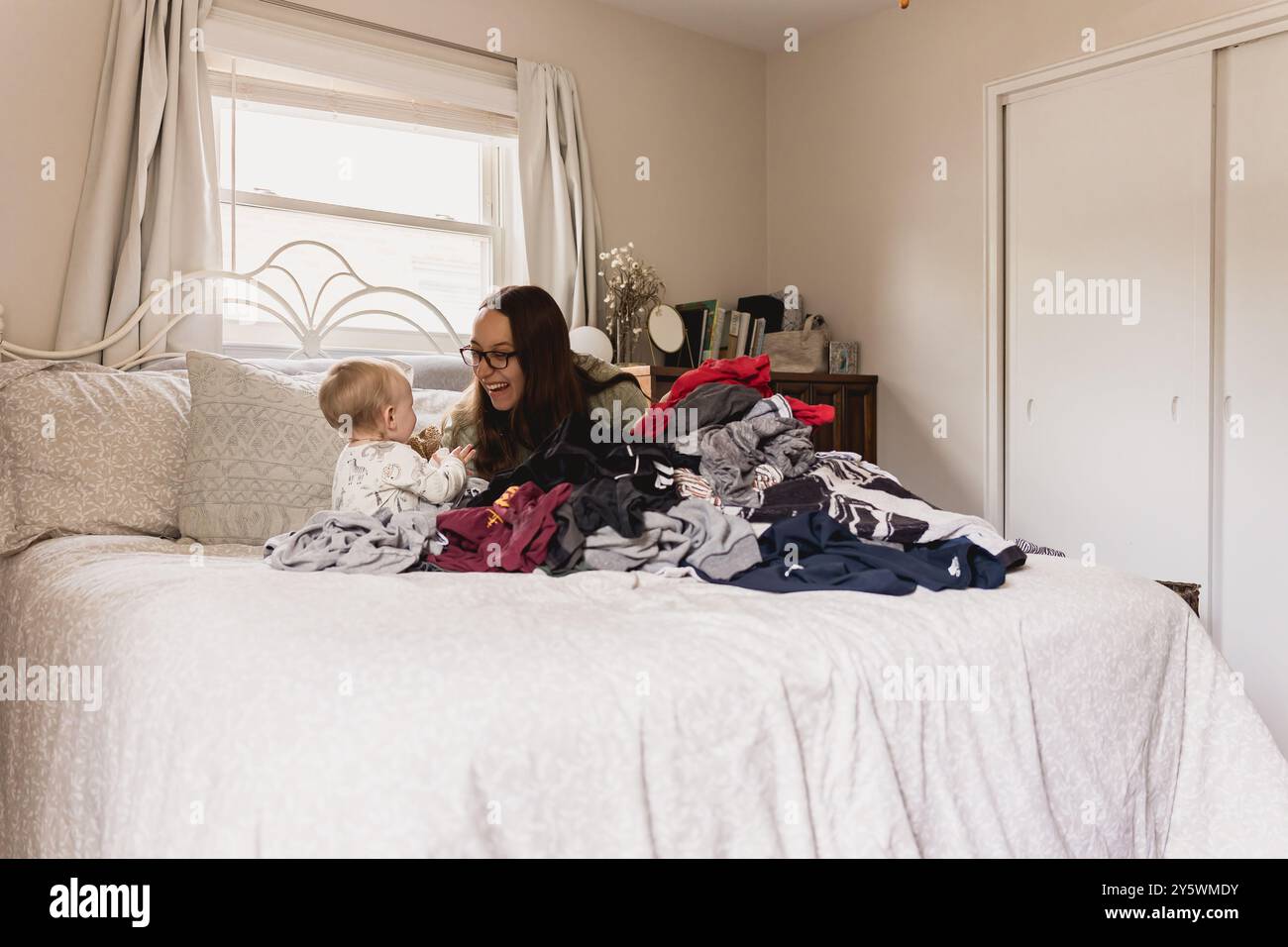 Mamma e bambino giocano su un letto circondato da un mucchio di bucato Foto Stock