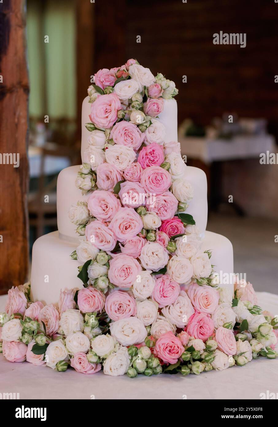 Una torta nuziale splendidamente decorata adornata con rose rosa e bianche in un ambiente interno rustico. Foto Stock