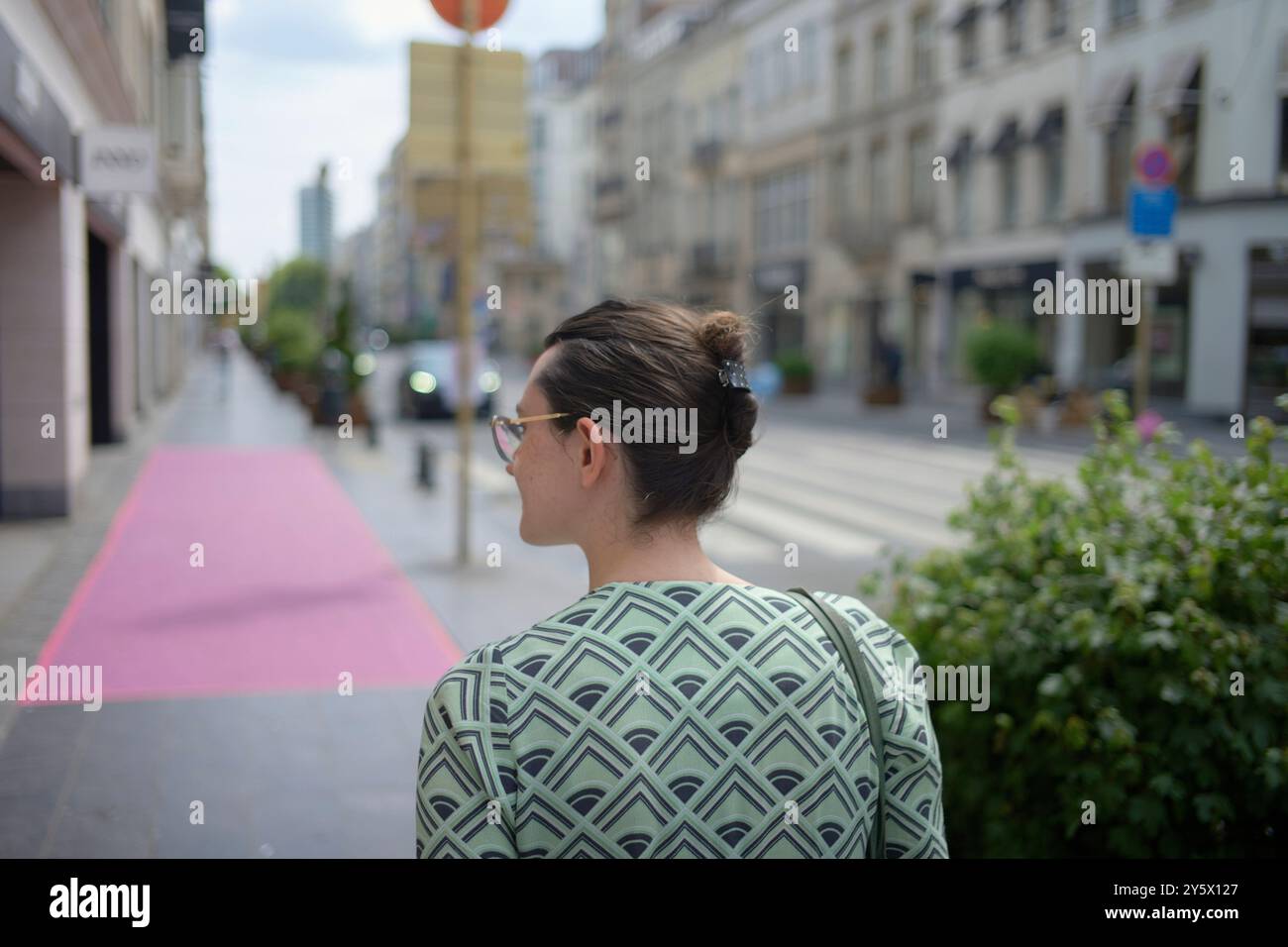 Donna con occhiali da sole che guarda alle spalle una strada della città con un vialetto rosa. Foto Stock