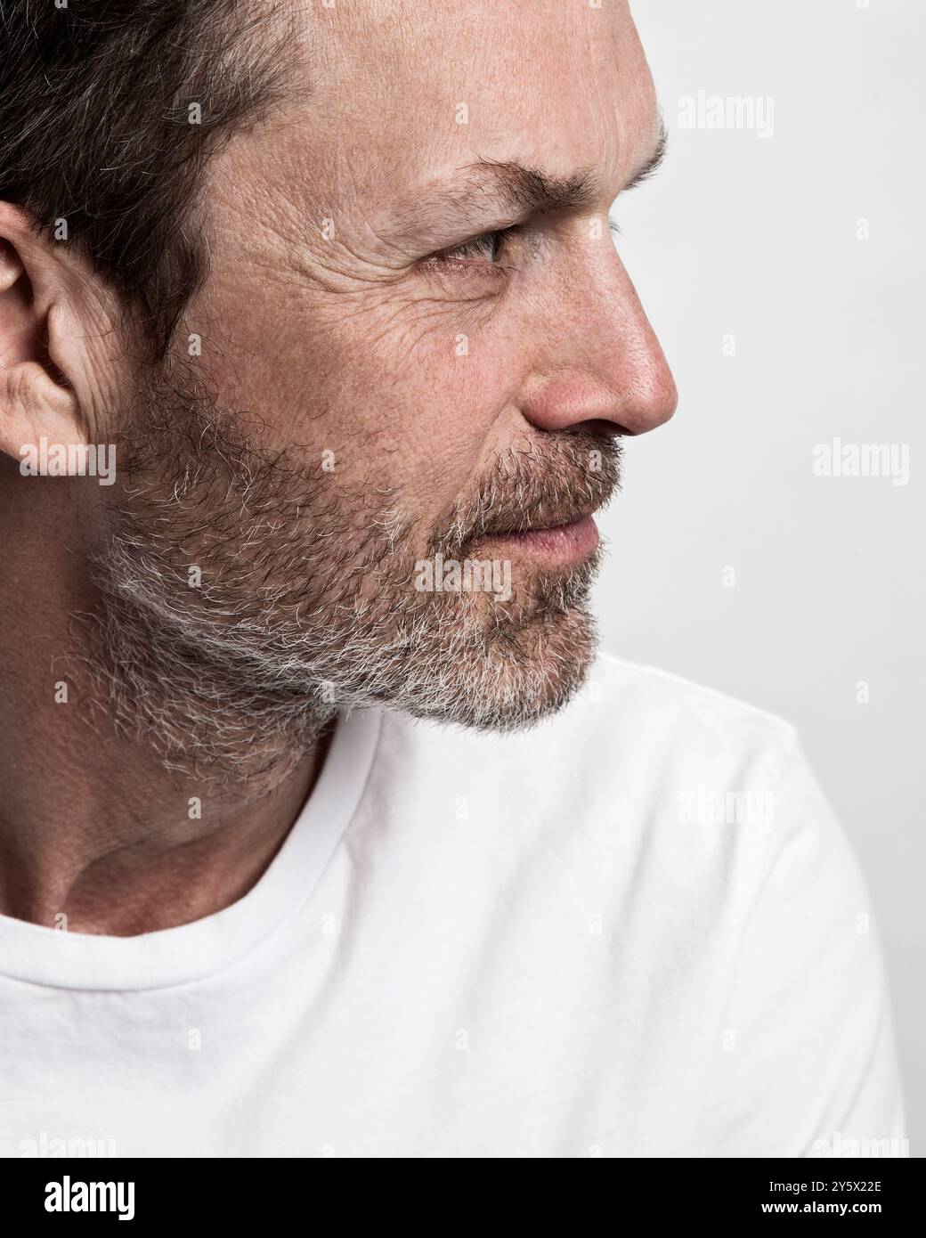 Profilo laterale di un uomo maturo con barba che indossa una T-shirt bianca su sfondo grigio. Foto Stock