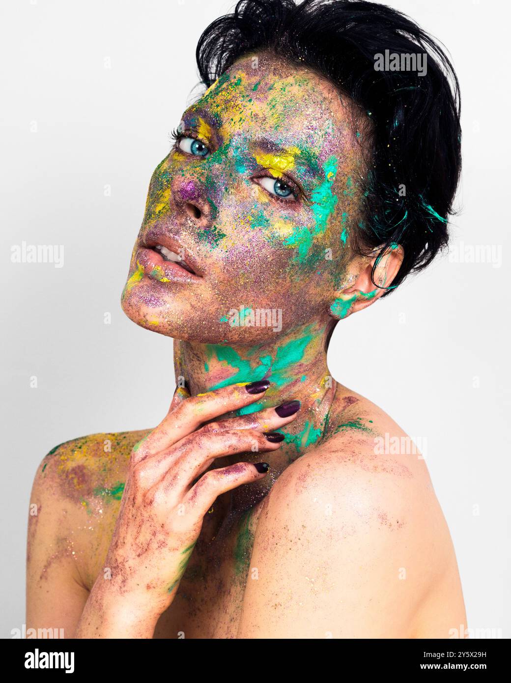 Donna con vernice colorata si schizza sul viso e sul corpo in posa su uno sfondo bianco. Foto Stock
