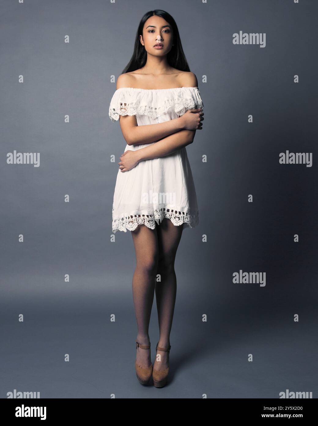 Elegante donna con abito bianco a spalla su sfondo grigio Foto Stock