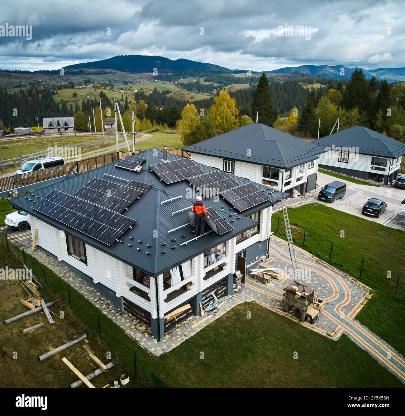 Ingegneri professionisti che installano batterie solari su un tetto di una grande casa in legno. Vista dei droni sull'installazione di pannelli solari in montagna. Concetto di elettricità verde. Foto Stock
