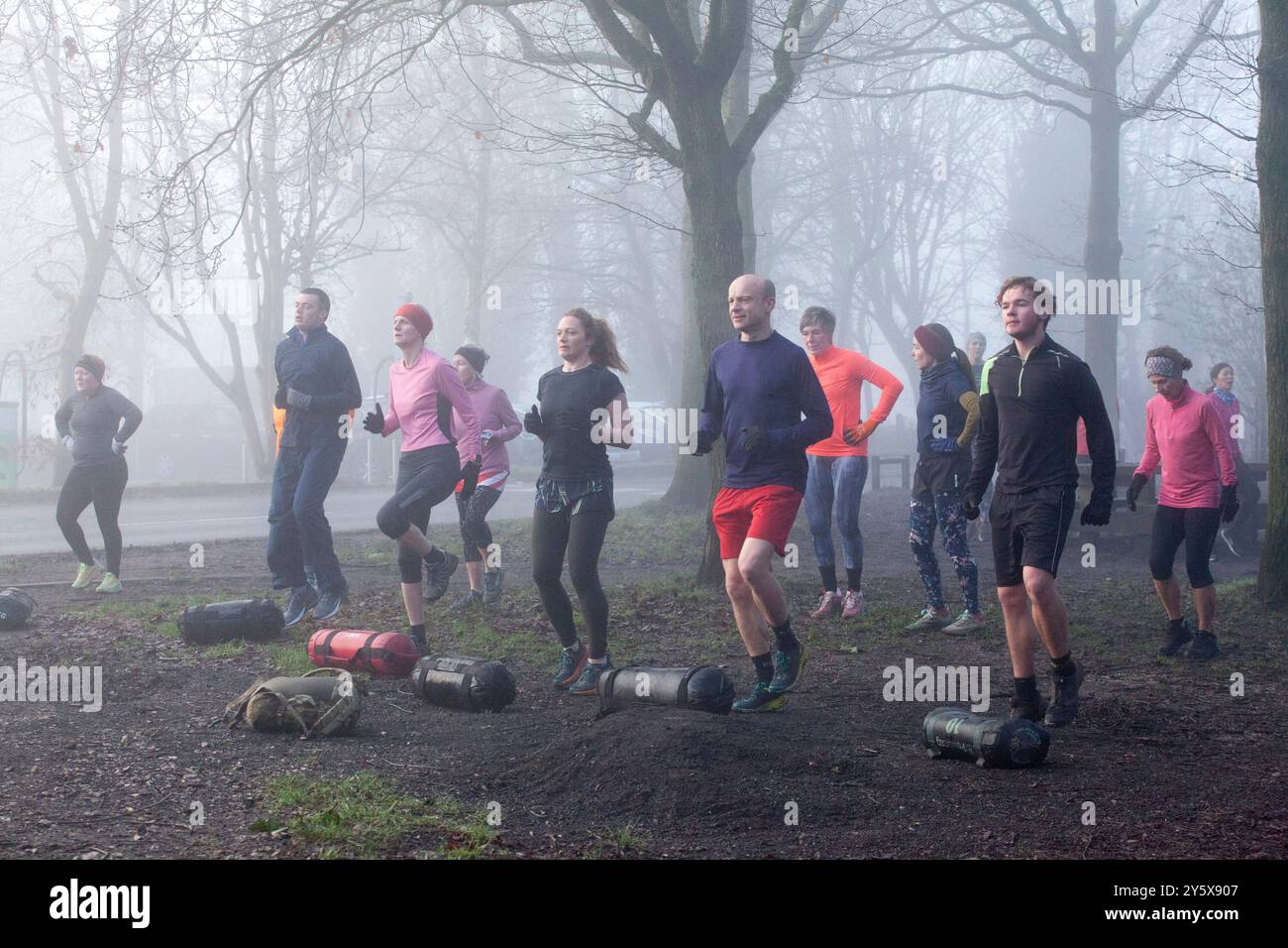 Gruppo di adulti impegnati in un bootcamp all'aperto in condizioni di nebbia, mostrando lavoro di squadra e fitness fisico. Foto Stock