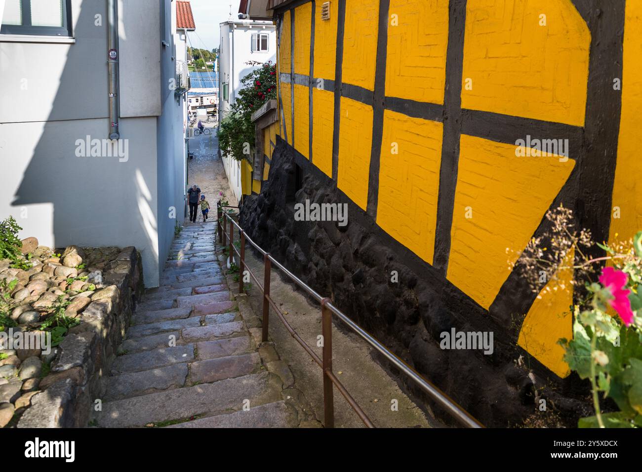 La ripida scalinata in pietra dal porto di Kappeln alla chiesa passa davanti a una casa a graticcio giallo e nero. Un adulto scende con un bambino. Schleswig-Holstein, Germania. Foto Stock