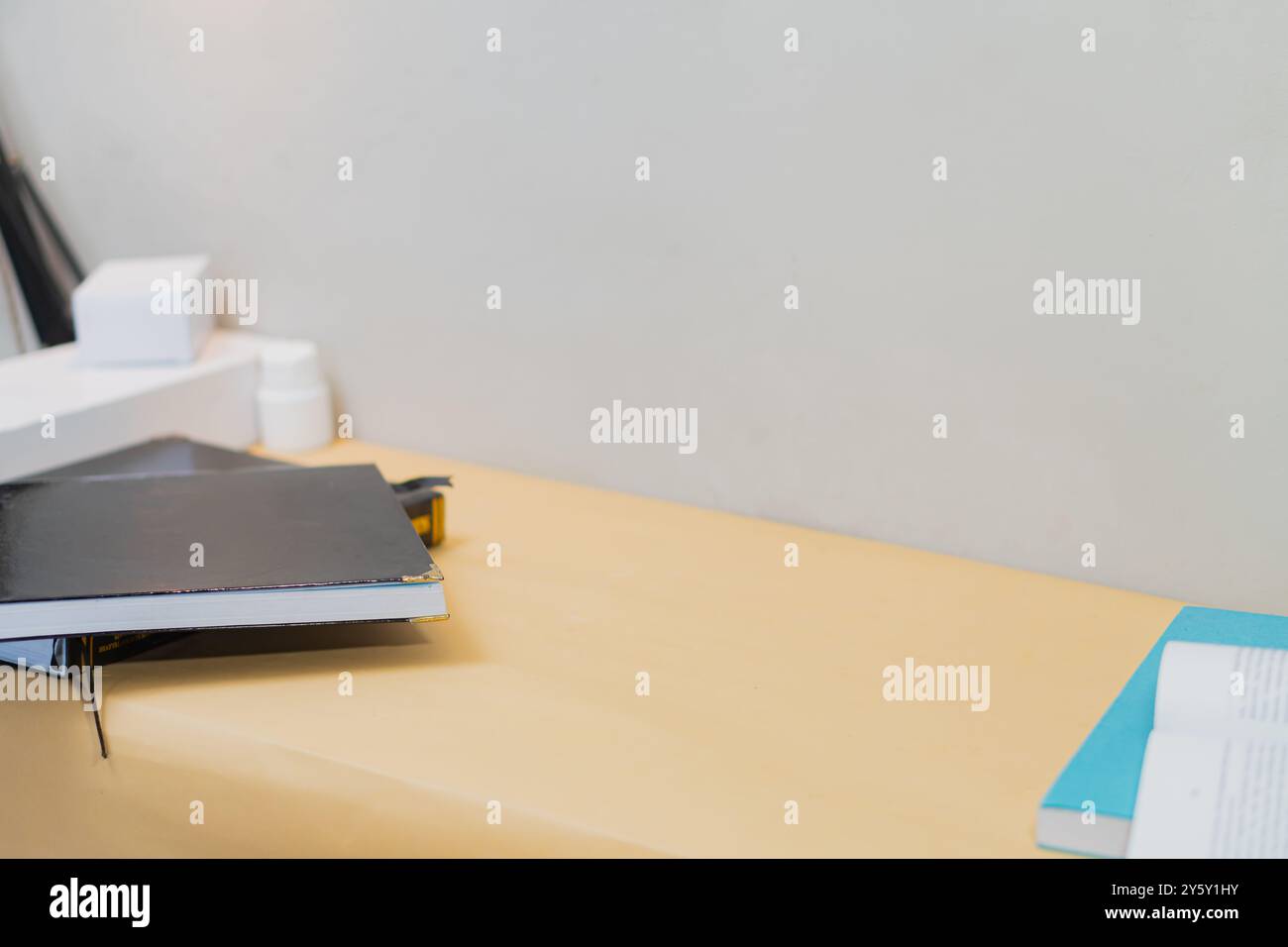 Uno spazio di lavoro pulito e minimalista con un notebook nero chiuso e un libro blu aperto su una scrivania di legno. Foto Stock