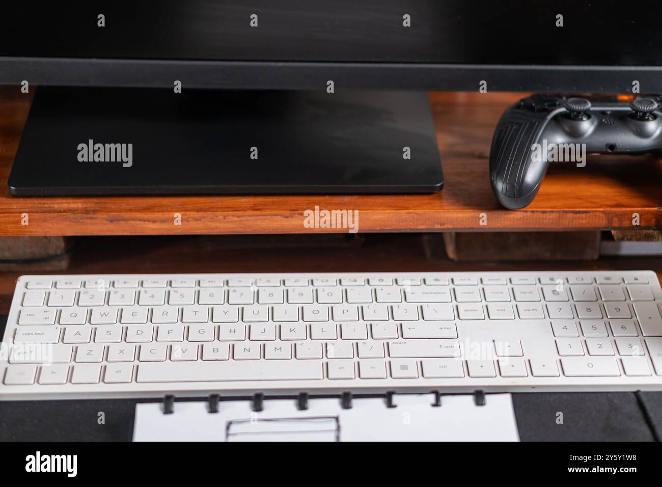 Una moderna configurazione da tavolo con tastiera e controller di gioco sotto un monitor, ideale per i videogame o la produttività. La superficie in legno aggiunge calore Foto Stock