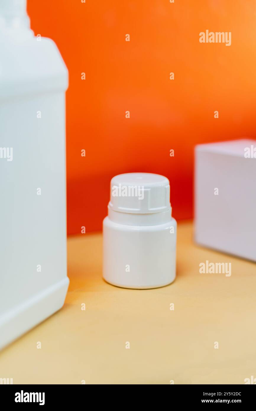 Primo piano di bottiglie di plastica bianche su una superficie leggera con un vivace sfondo arancione, che mostra il design e la confezione del prodotto in uno stile minimalista. Foto Stock
