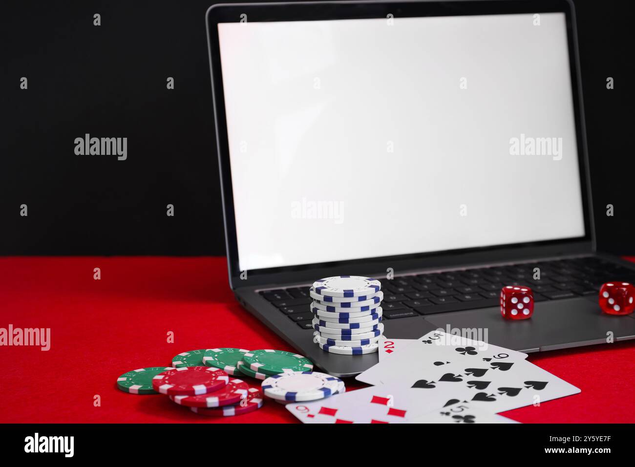 Laptop, patatine da poker, carte da gioco e dadi sul tavolo rosso. Gioco online Foto Stock