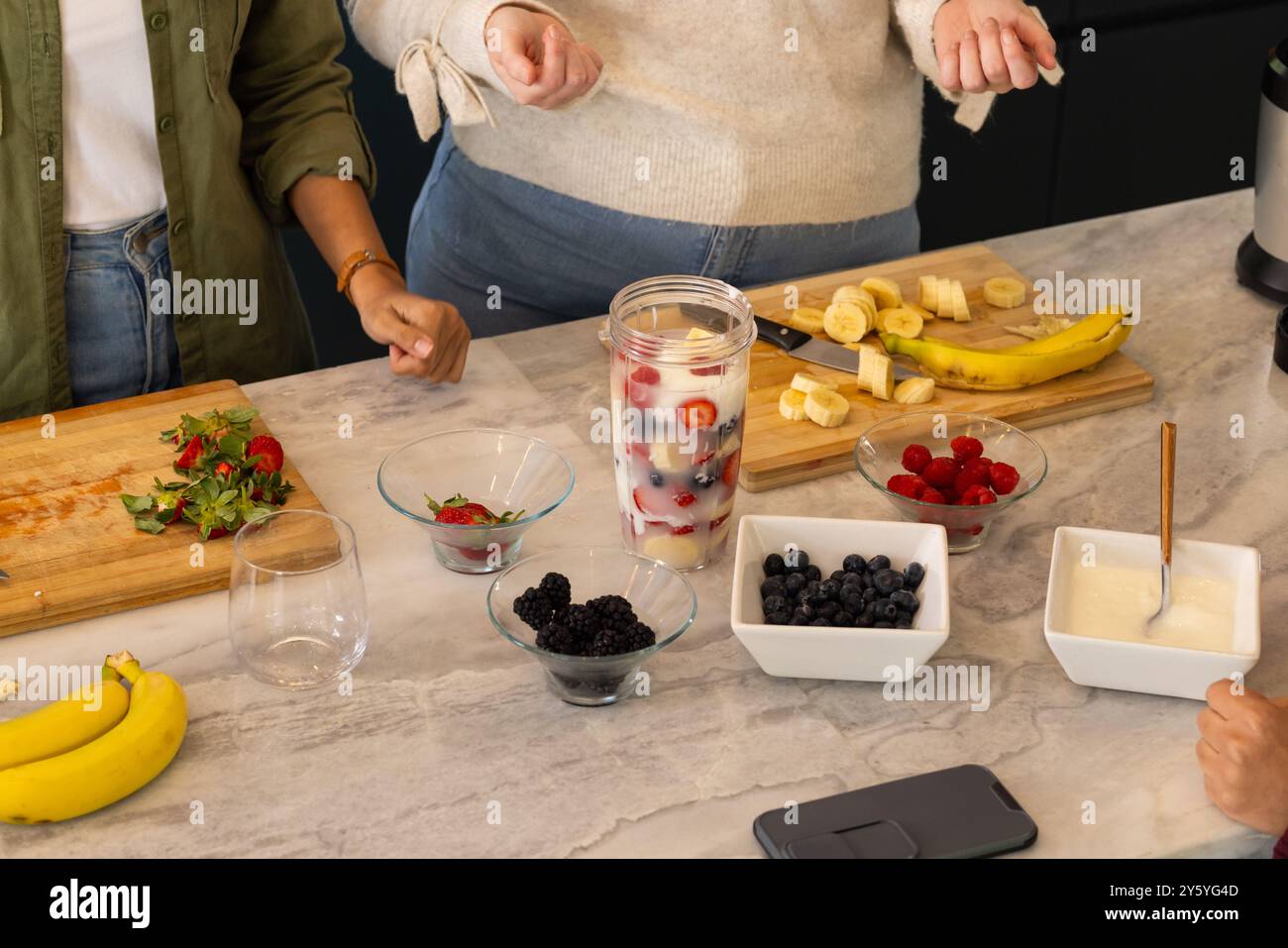 Tritare la frutta e mescolare gli ingredienti, gli amici preparano frullati di frutta fresca insieme Foto Stock