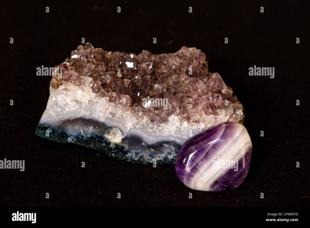 Cristalli di un geode di Ametista insieme a una pietra di Ametista lucidata su sfondo nero Foto Stock