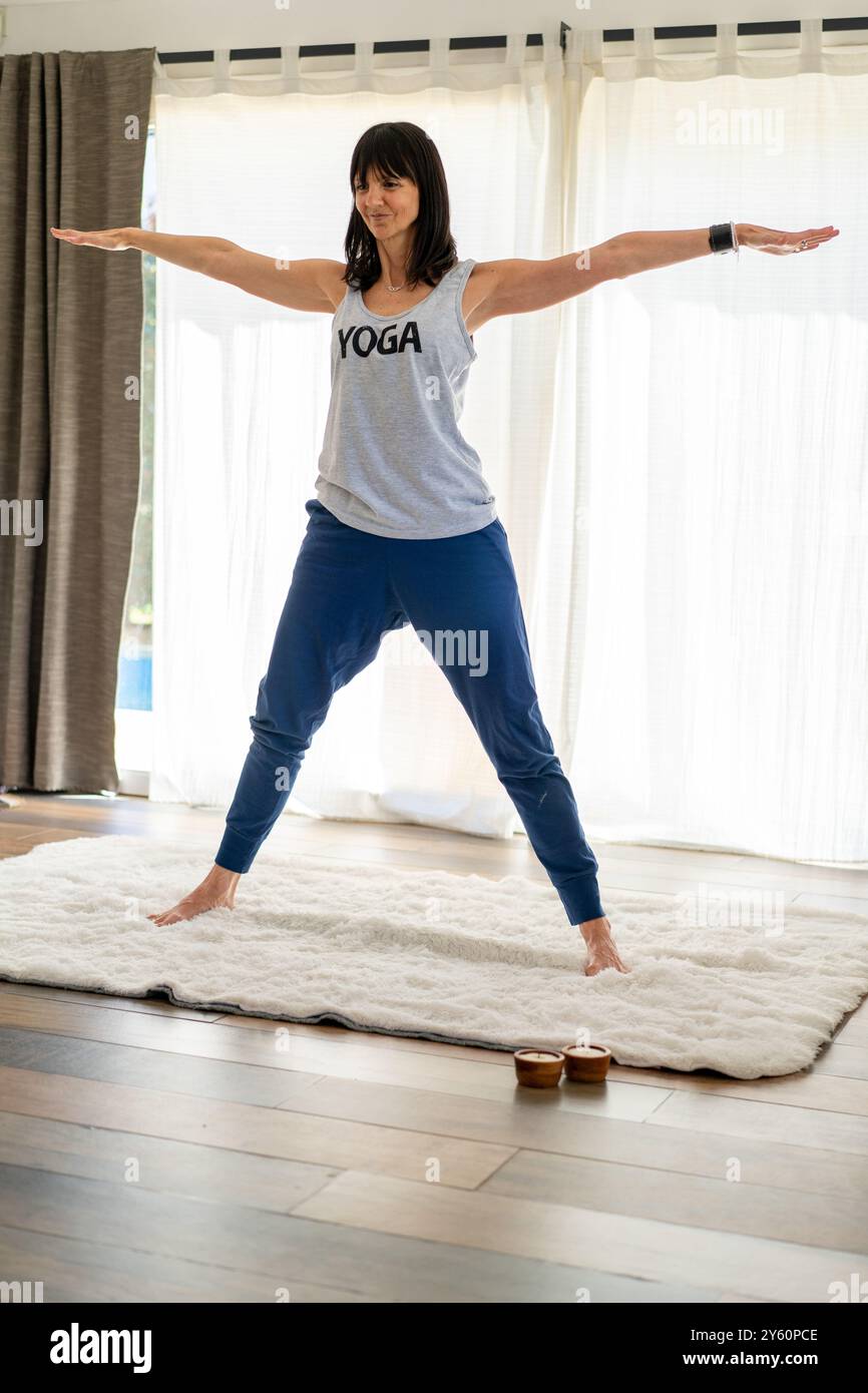 Istruttore di yoga alla moda che dondola una canotta grigia con "YOGA" mentre mostra la posa DELLE STELLE. Foto Stock