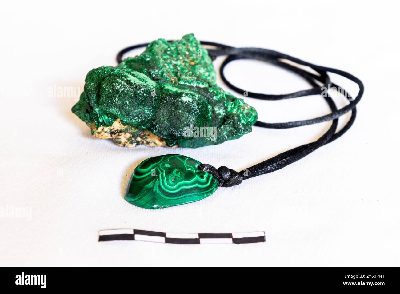 Una collana unisex con una singola pietra di malachite lucida con un campione ruvido di malachite su sfondo bianco con una scala di 5 mm Foto Stock