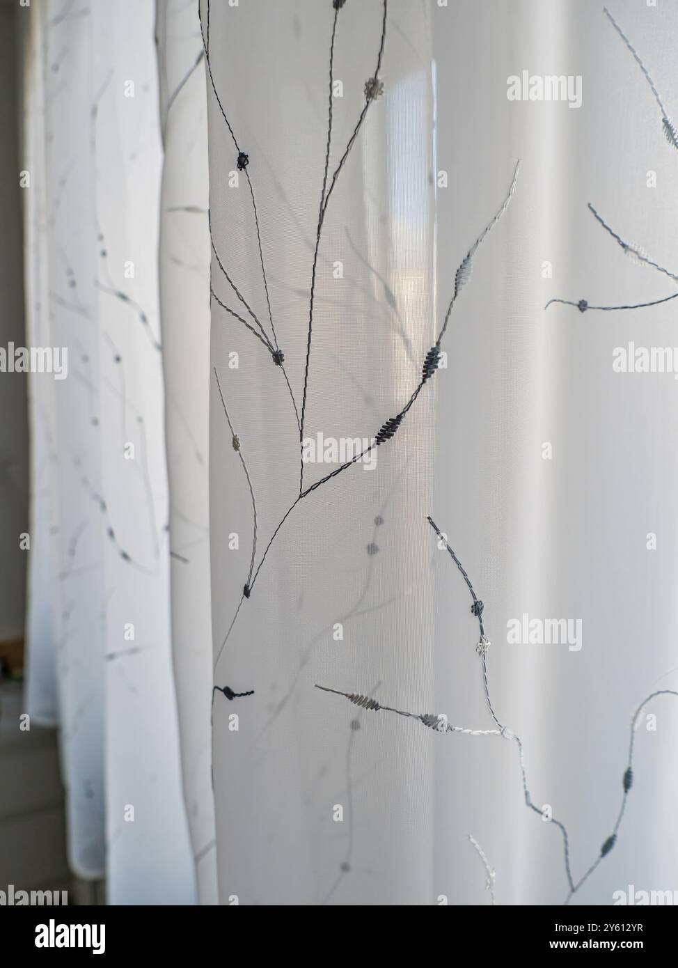 Primo piano di tende bianche e trasparenti ornate da sottili ricami botanici, che filtrano delicatamente la luce. Perfetto per l'elegante decorazione degli interni che migliora un Foto Stock