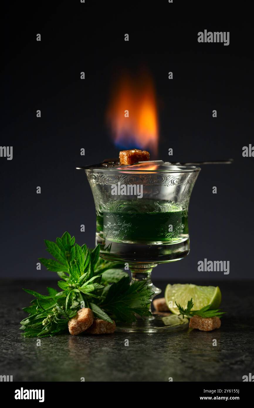 Bruciare lo zucchero su un bicchiere con assenzio. Preparazione della bevanda. Absinthe con ingredienti su sfondo nero. Foto Stock