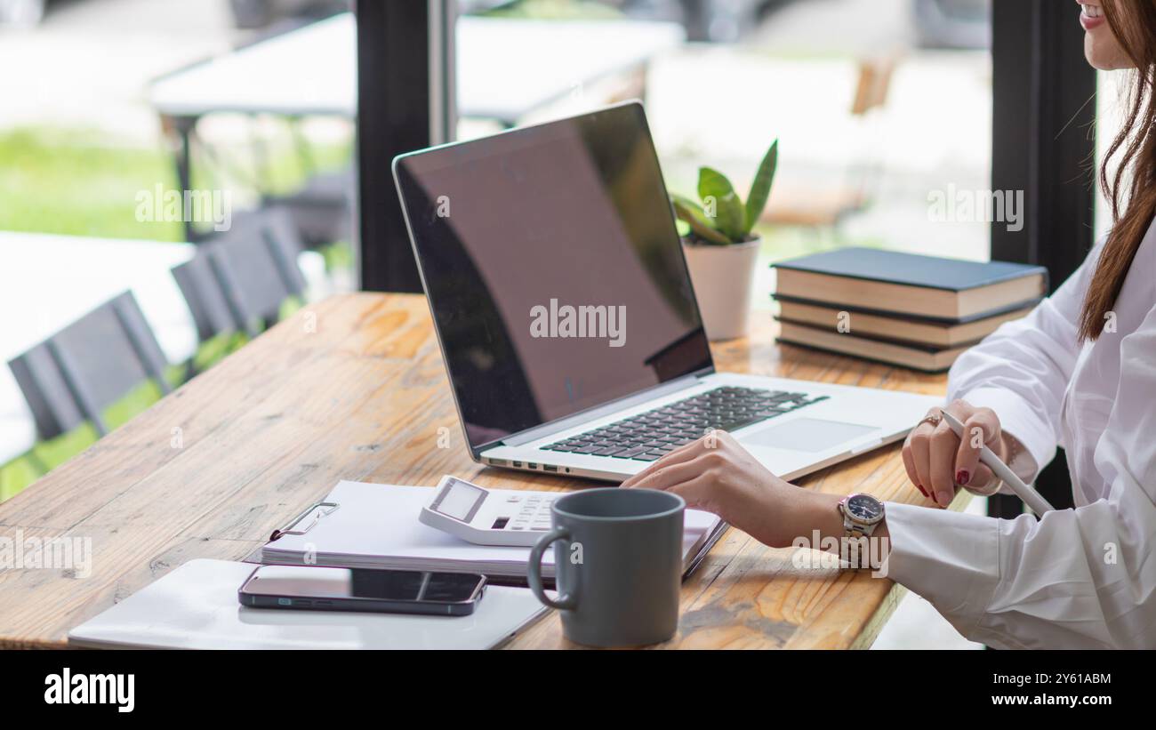 Una giovane donna d'affari sta esaminando i risultati della rete aziendale tramite computer portatili e Internet al fine di preparare documenti per le riunioni da offrire agli investitori Foto Stock