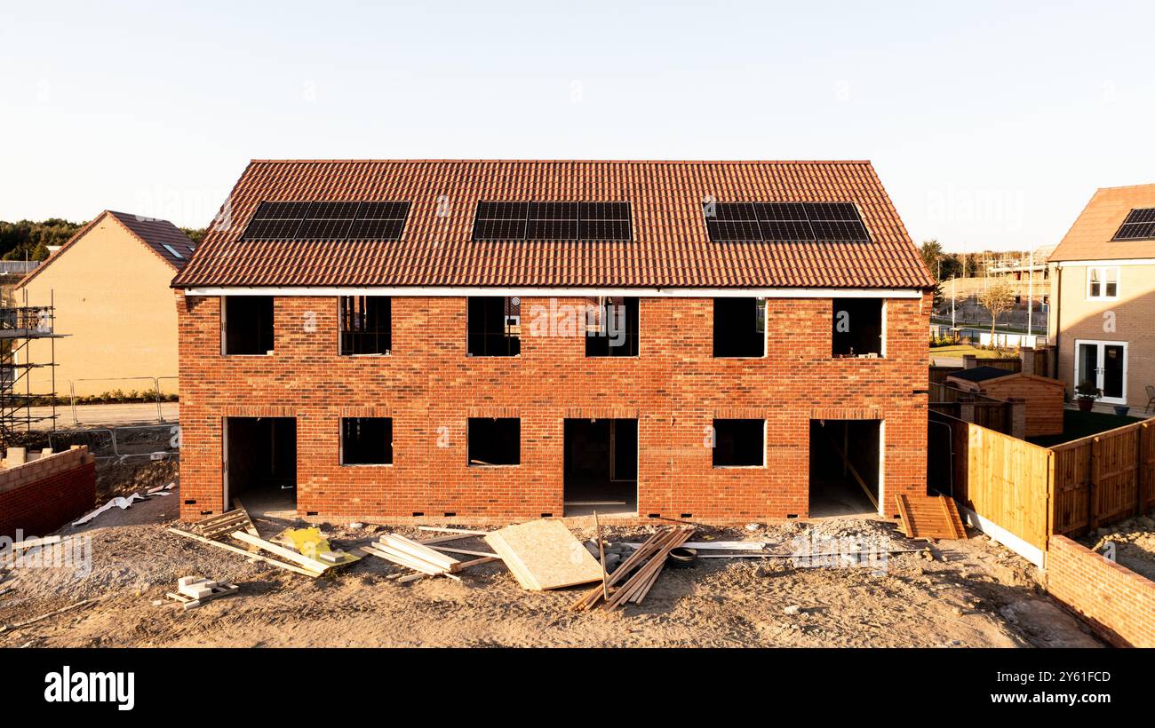 Una fila di case di nuova costruzione parzialmente costruite in un cantiere con tetto integrato o pannelli solari integrati nel tetto per un'energia economica e sostenibile in una e Foto Stock