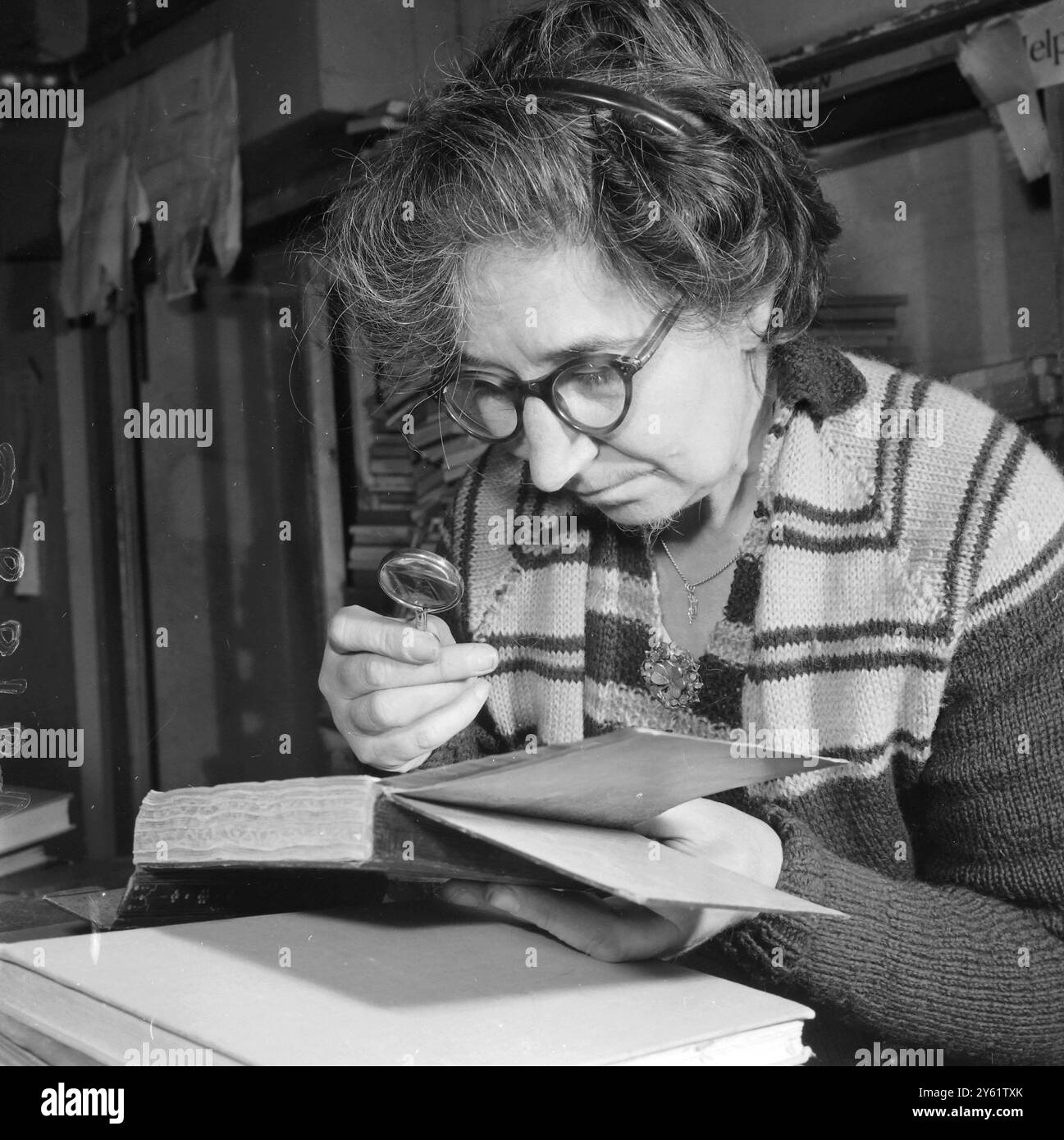 UTILIZZANDO UNA LENTE D'INGRANDIMENTO SI TROVA LILIAN MANNING, L'ACQUIRENTE DI LIBRI DI SECONDA MANO PER LA LIBRERIA FOYLES, LA PIÙ GRANDE LIBRERIA BRITANNICA A CHARING CROSS ROAD, LONDRA, 11 FEBBRAIO 1960 Foto Stock