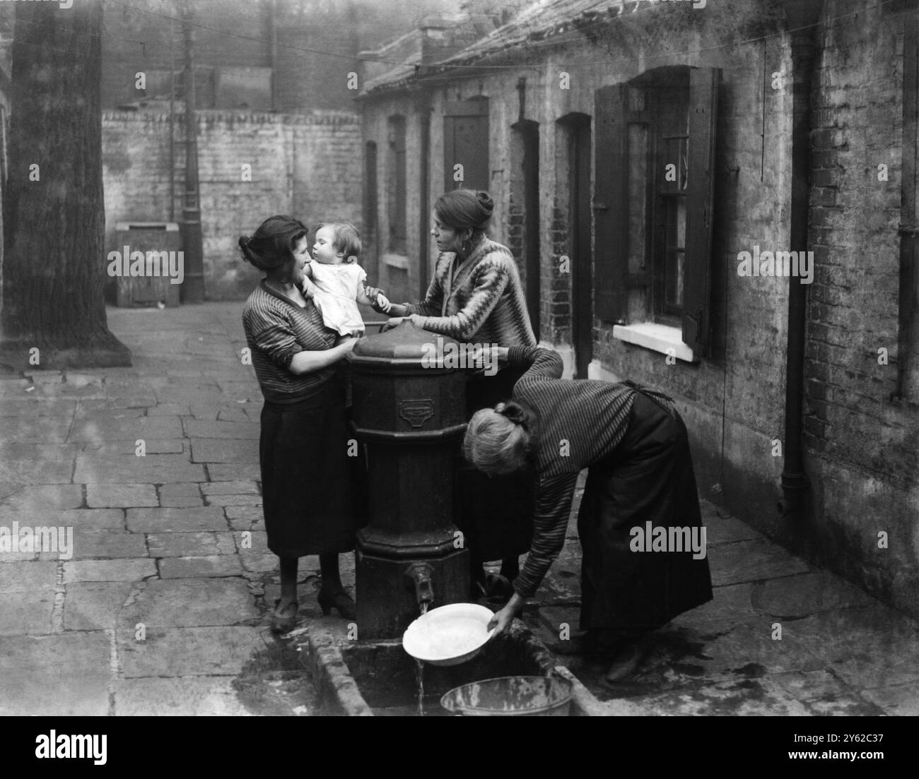 Newton 's affitta da Twine Court a Shadwell - il centro di una delle peggiori baraccopoli di Stepney , Londra . Quando l'immagine delle tre donne e del bambino intorno alla pompa comune - condivisa da undici famiglie fu pubblicata su The Star nel 1931 , ci fu un grido pubblico e i cottage furono demoliti e sostituiti dallo schema Ring House del Consiglio Stepney ©TopFoto Foto Stock