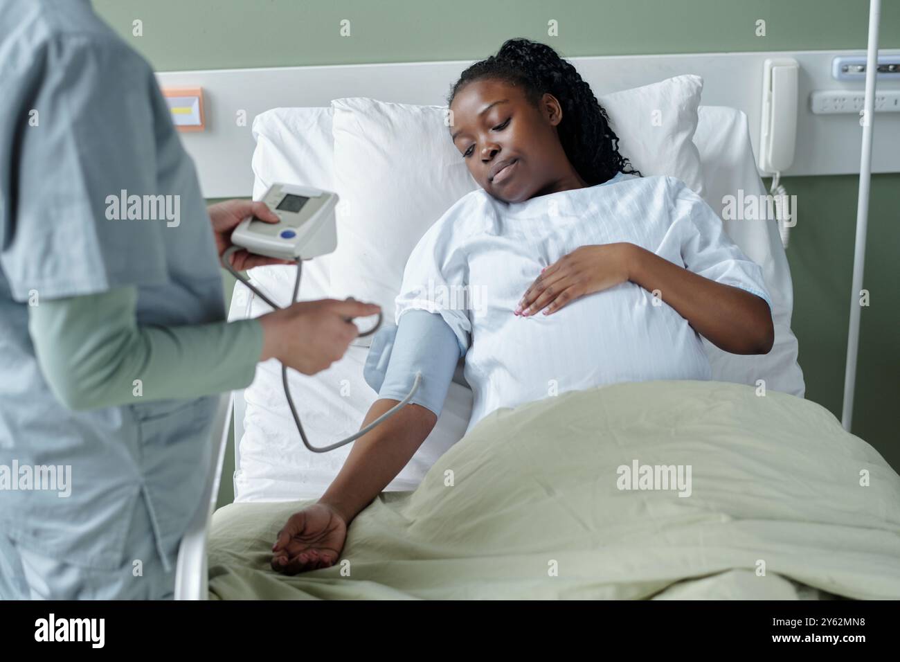 Medico che misura la pressione sanguigna della donna incinta in posizione letto d'ospedale. Donna che riposa con calma mentre il processo sanitario è in corso Foto Stock