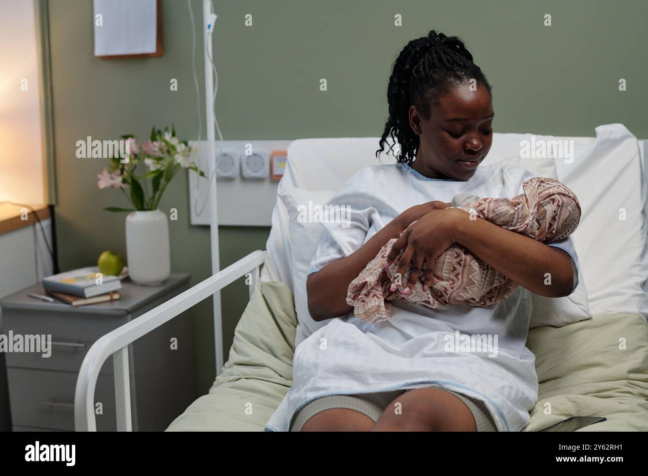Madre premurosa che tiene il neonato mentre è seduta sul letto d'ospedale in reparto di maternità guarda delicatamente il bambino con affetto e tenerezza madre piena di emozione Foto Stock