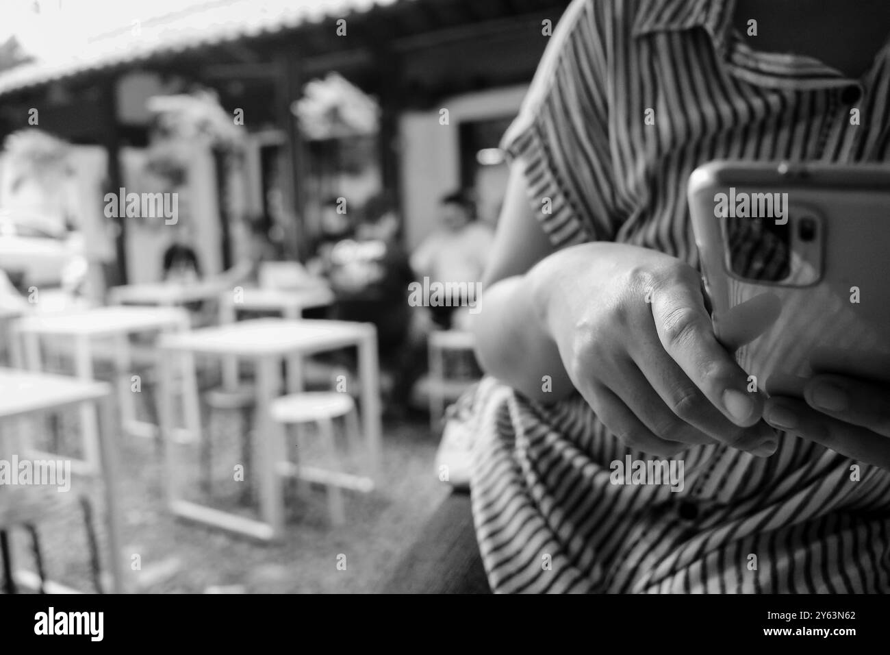 Donna adulta che indossa la parte superiore a righe con smartphone e ristorante all'aperto sullo sfondo Foto Stock